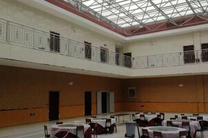 Un amplio salón interior con techo alto, varias mesas y sillas, y un balcón en el nivel superior.