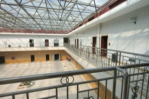 Un vaste espace intérieur doté d’un haut plafond et d’un toit en verre, comprenant plusieurs portes et un espace central ouvert.