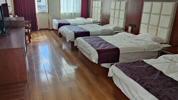 Habitación de hotel con tres camas, piso de madera, un escritorio y una ventana con cortinas.
