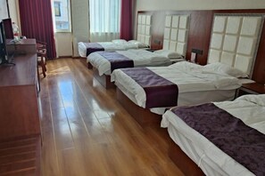 Une chambre d’hôtel avec trois lits, un plancher en bois, un bureau et une fenêtre avec des rideaux.