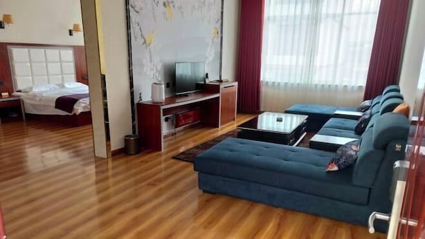 Une chambre d’hôtel avec un plancher en bois, un canapé bleu, une télévision, un lit et un rideau rouge.