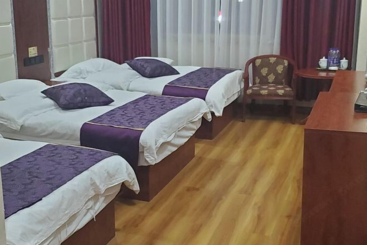 Une chambre d’hôtel avec deux lits, un plancher en bois, une petite table ronde avec une chaise et une fenêtre avec des rideaux.