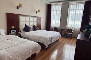 A hotel room with two beds, a wooden floor, a desk with a chair, and a window with curtains. - Kangma Weinasi Hotel (Kangma)