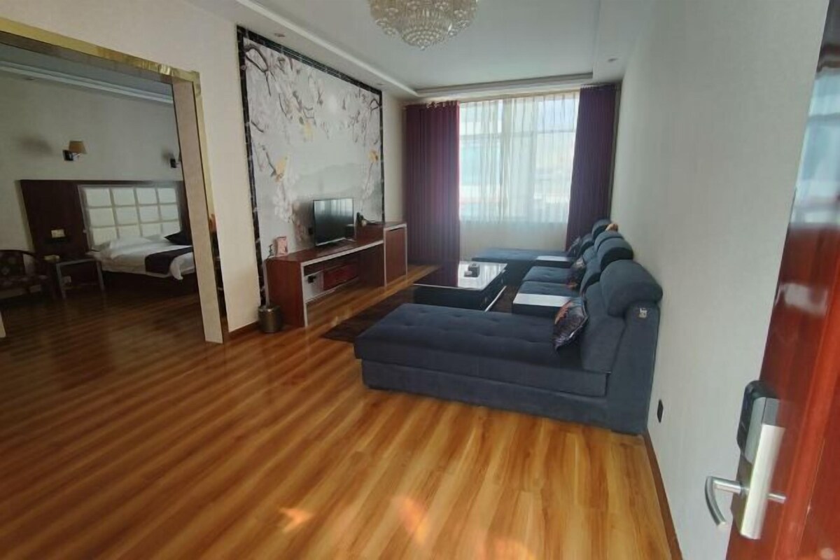 Un salon moderne avec un plancher en bois, un canapé bleu foncé, un téléviseur à écran plat et une grande fenêtre avec des rideaux.