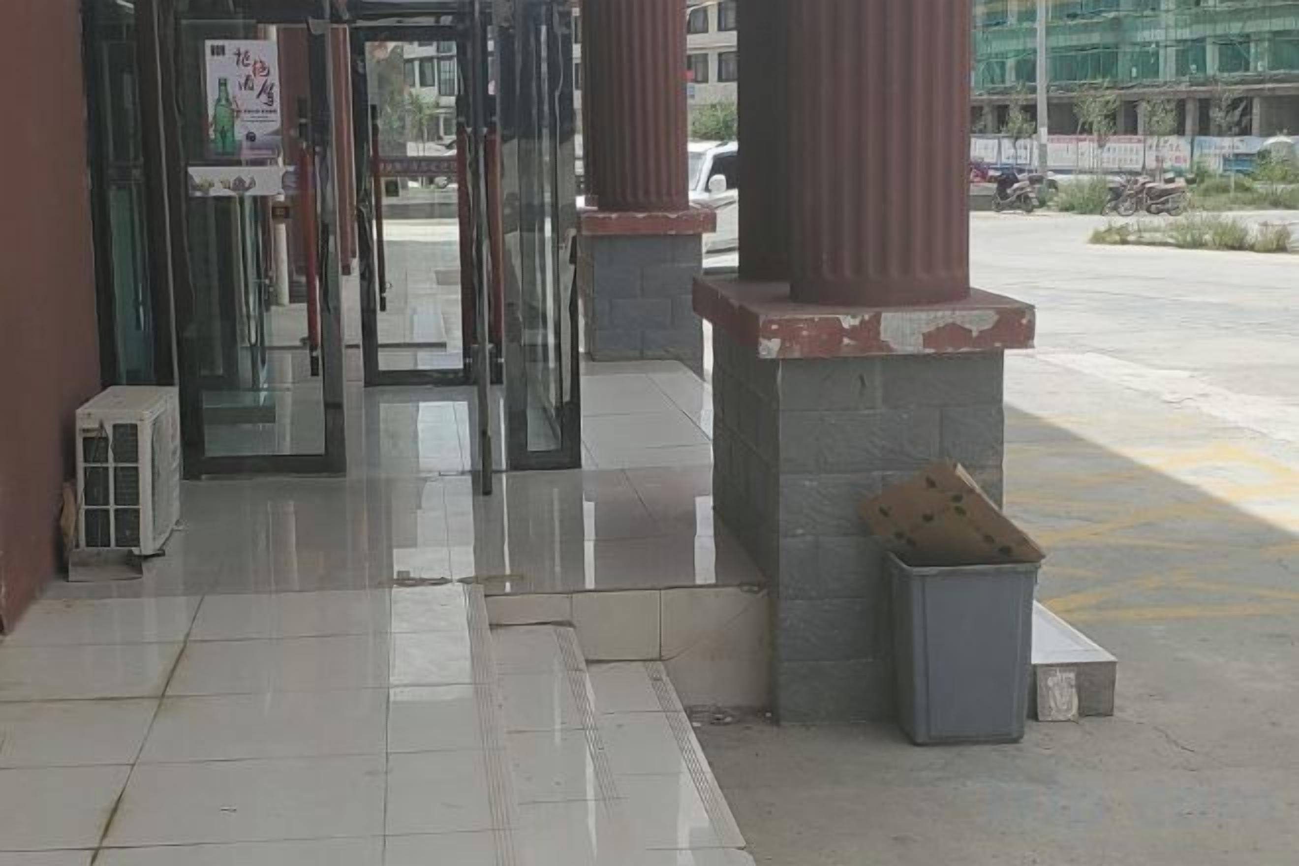 A building entrance with glass doors, a trash bin, and a clear view of the street outside.