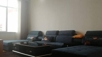 A living room with a sectional sofa, a coffee table, and a window with curtains.