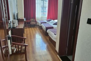 A hotel room with a wooden floor, two beds with purple bedding, a desk with a chair, and a window with red curtains. - Kangma Weinasi Hotel (Kangma)