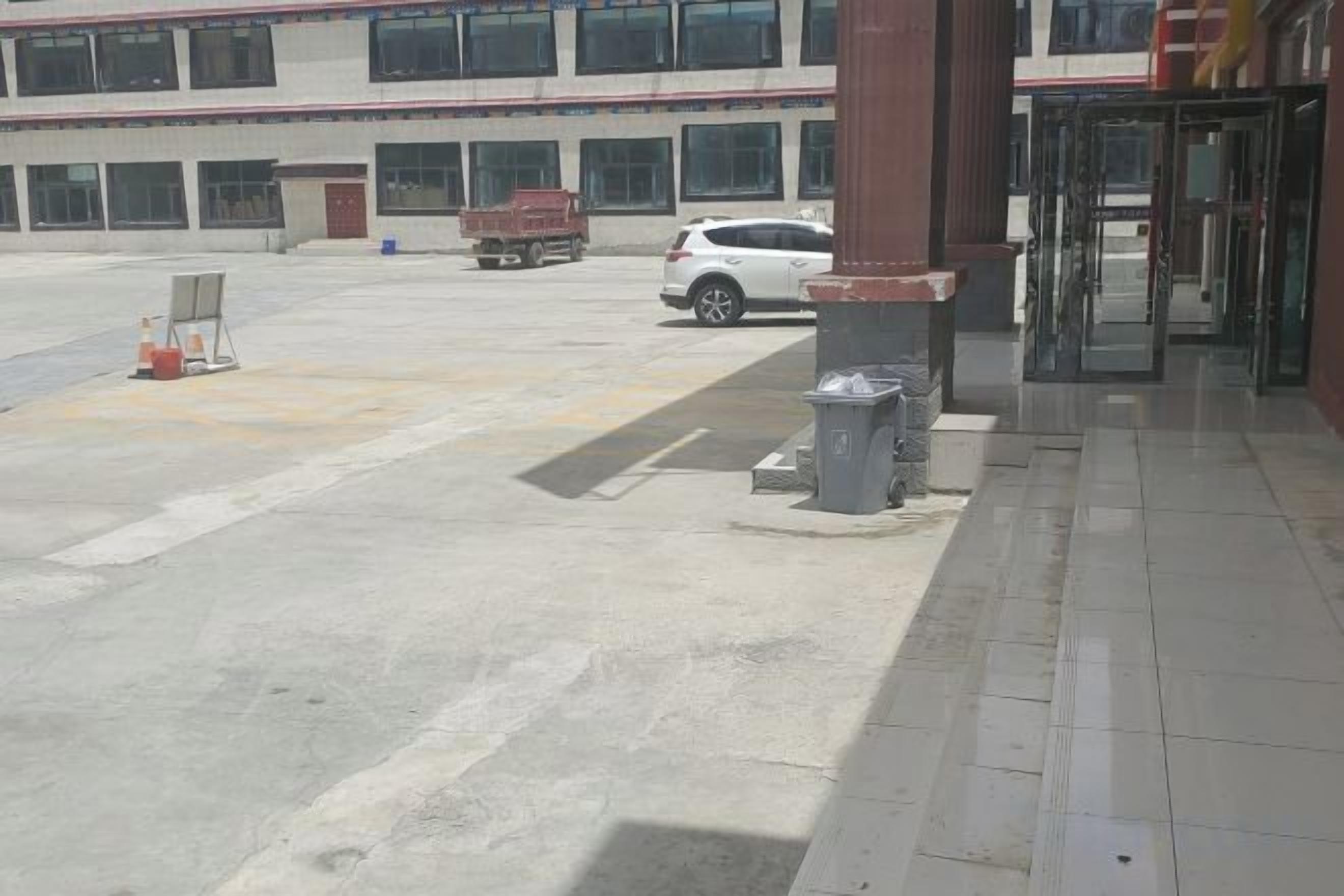 A building entrance with a paved driveway, a turnstile, and a parked white vehicle.