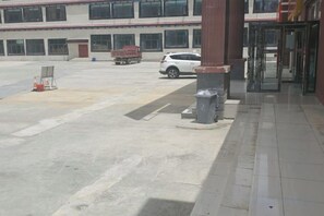 A building entrance with a paved driveway, a turnstile, and a parked white vehicle. - Kangma Weinasi Hotel (Kangma)