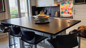 A modern kitchen with a central island, pendant lighting, and a colorful decorative piece on the wall. - House with sea view next to the beach (Trouville-sur-Mer)