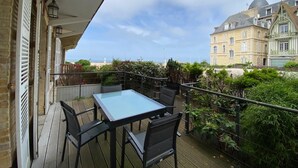 A balcony with a table and chairs, overlooking a beach and buildings. - House with sea view next to the beach (Trouville-sur-Mer)