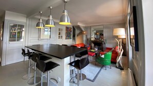 A modern kitchen with a central island, bar stools, pendant lighting, and a dining area with a red sofa. - House with sea view next to the beach (Trouville-sur-Mer)