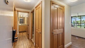 A hallway with wooden doors, a kitchen area, and a window with a view of palm trees. - Maui Sunset Vacation Rentals A419 (Kihei)