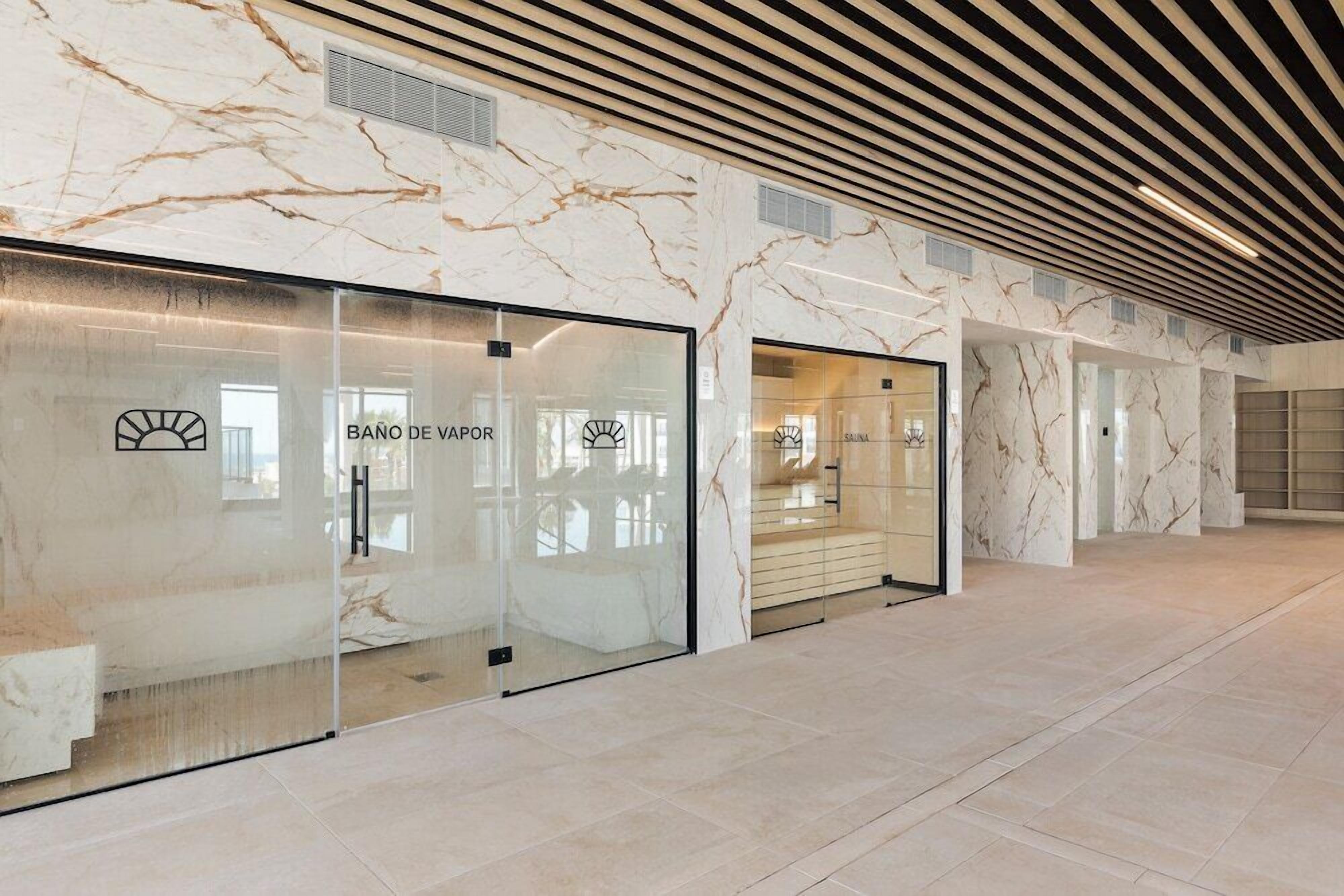 A modern interior with marble walls, a glass door entrance, and a ceiling with wooden slats.