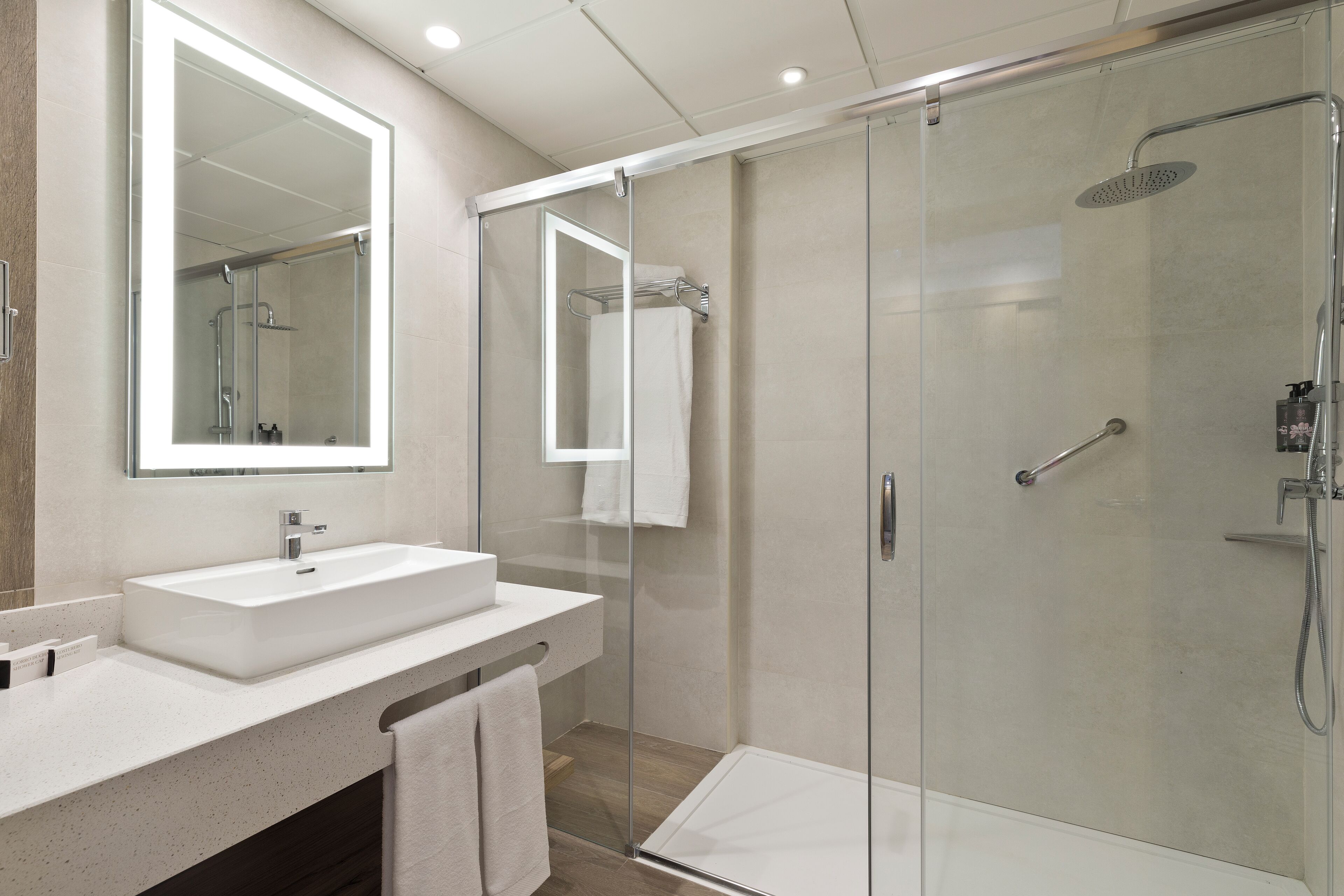 Un baño moderno con ducha de vidrio, un espejo grande y un lavabo blanco.