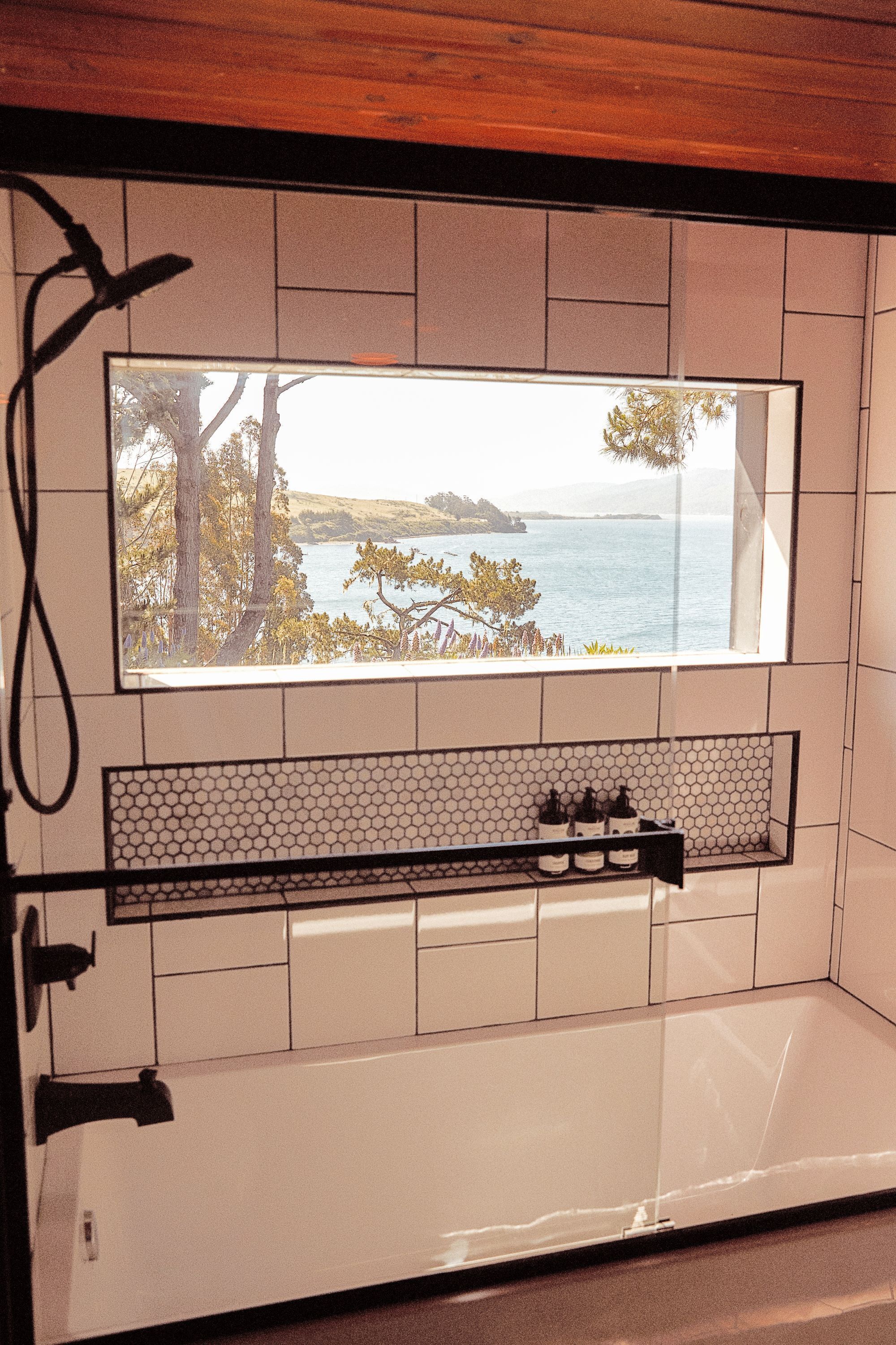 A bathroom with a large mirror, a sink with a hexagonal tile backsplash, and a view of the sea through the window.