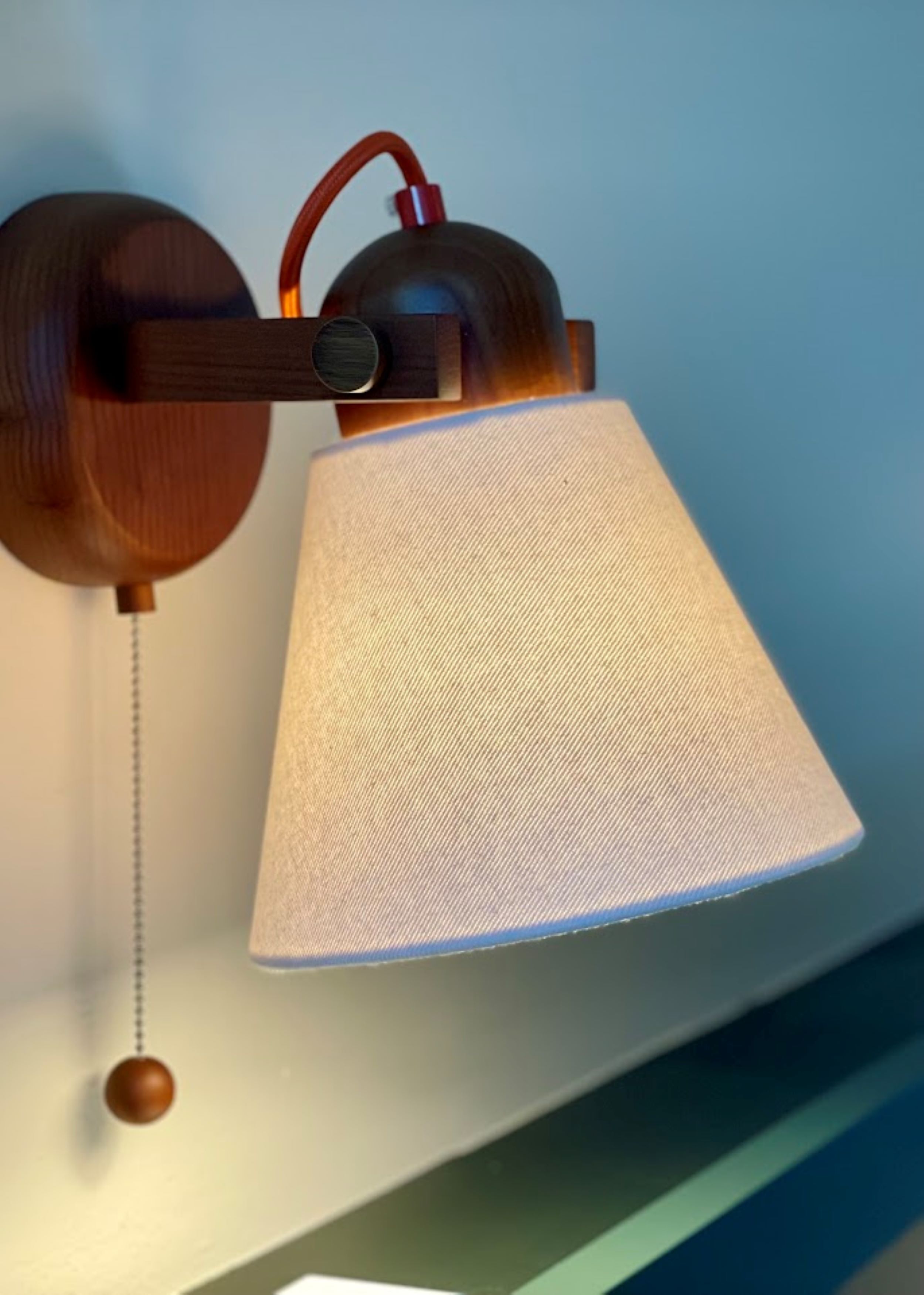 A wall-mounted lamp with a conical shade and a hanging bulb.
