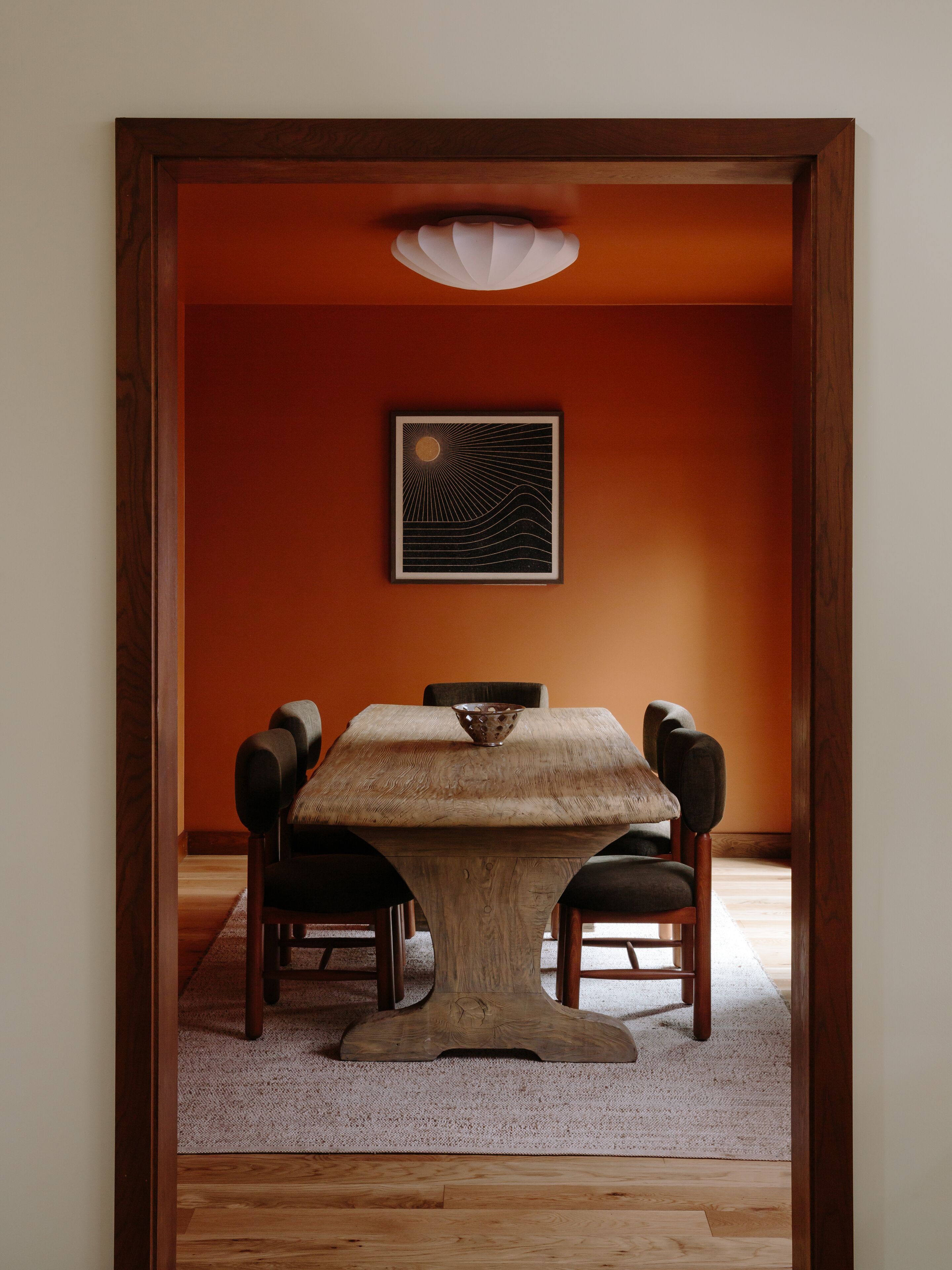 A dining area with a wooden table and chairs, a framed artwork on the wall, and a carpeted floor.