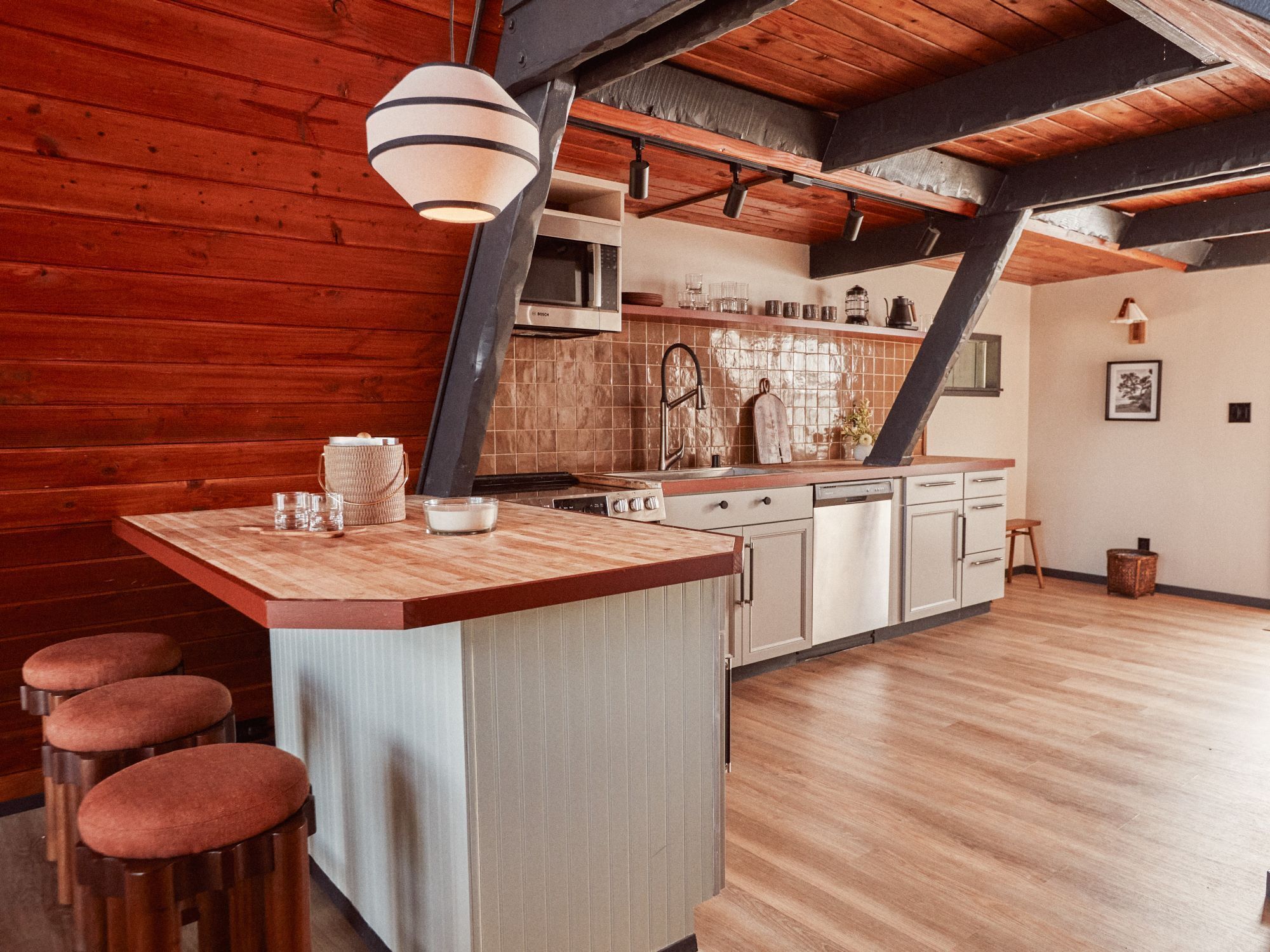 A kitchen with a wooden island, bar stools, and a hanging light fixture.