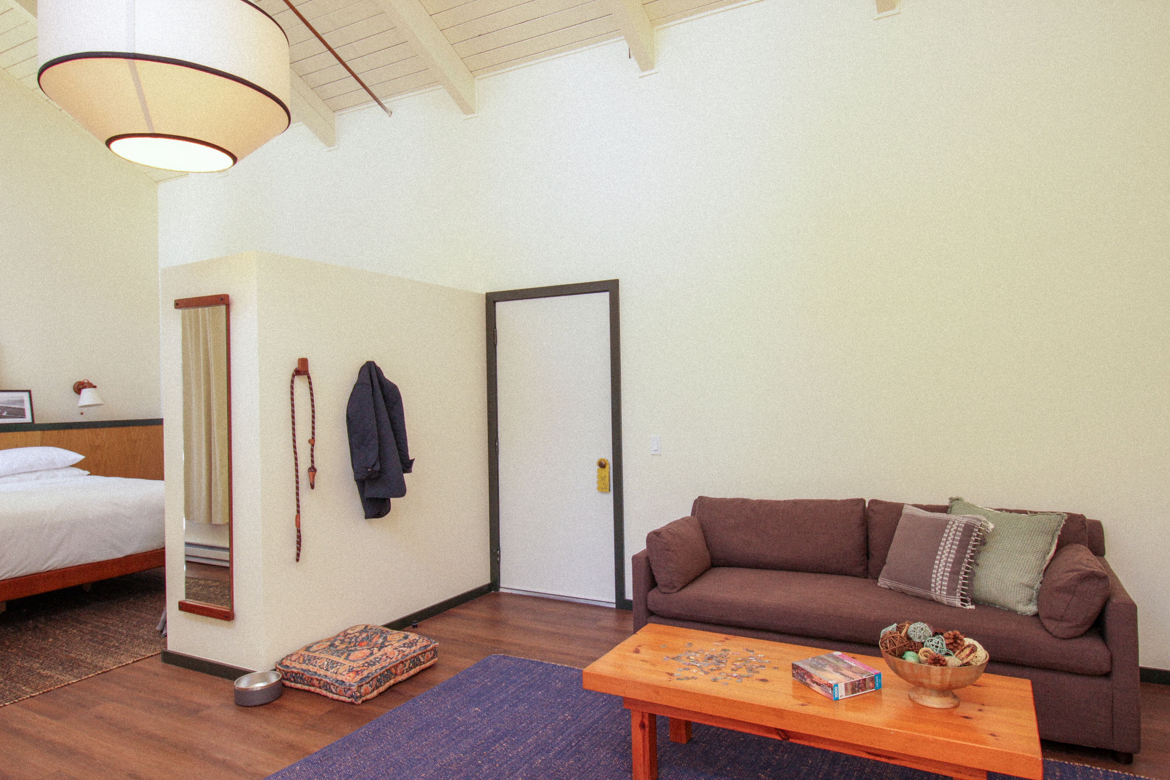 A room with a bed, a brown sofa, a wooden coffee table, and a door.
