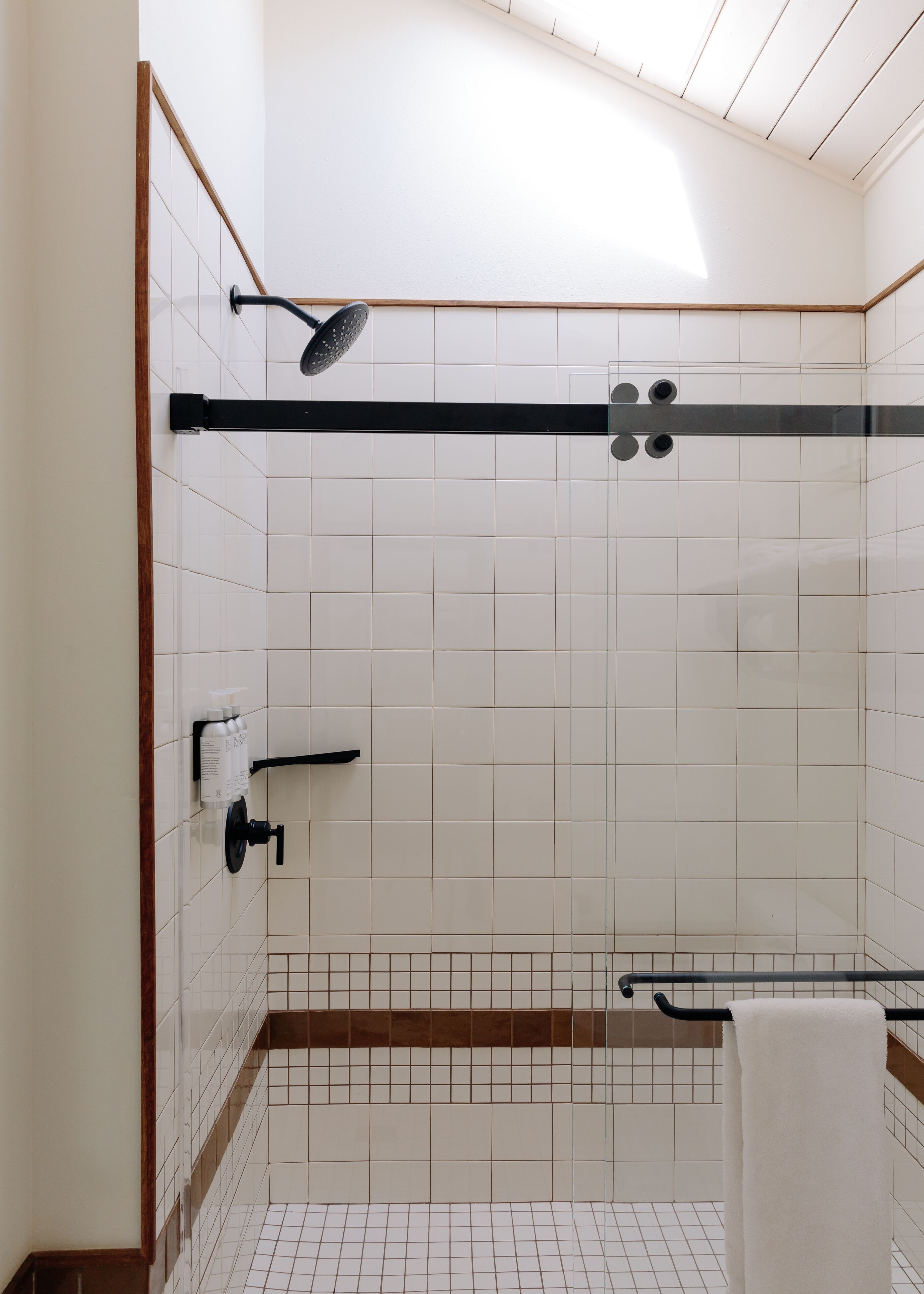Un baño moderno con paredes de azulejos blancos, una zona de ducha con marco de madera y un perchero.