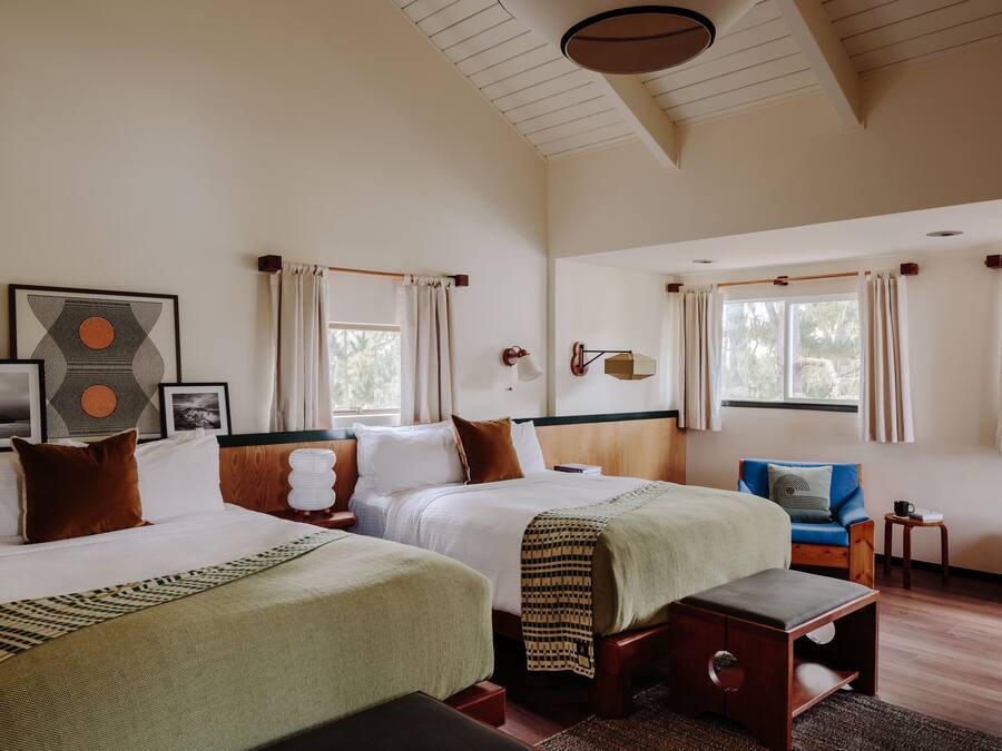 A hotel room with two beds, a small seating area, and a window with curtains.