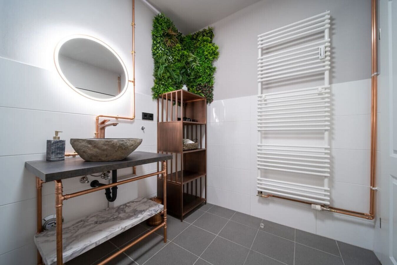 Ein modernes Badezimmer mit einem runden Spiegel, einem Becken aus Stein, Kupferrohren, einer grünen Wand und einem weißen Heizkörper.