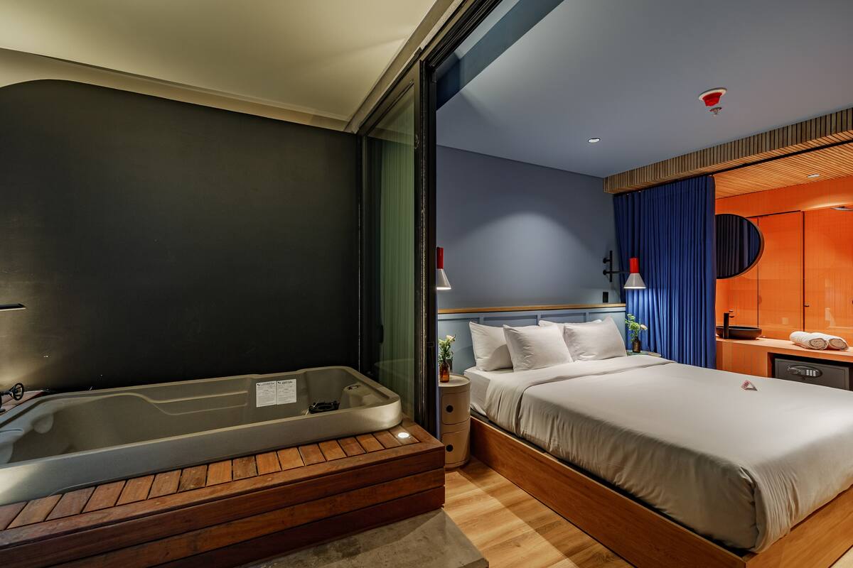 A modern hotel room with a large bed, a built-in bathtub, and a wooden floor.