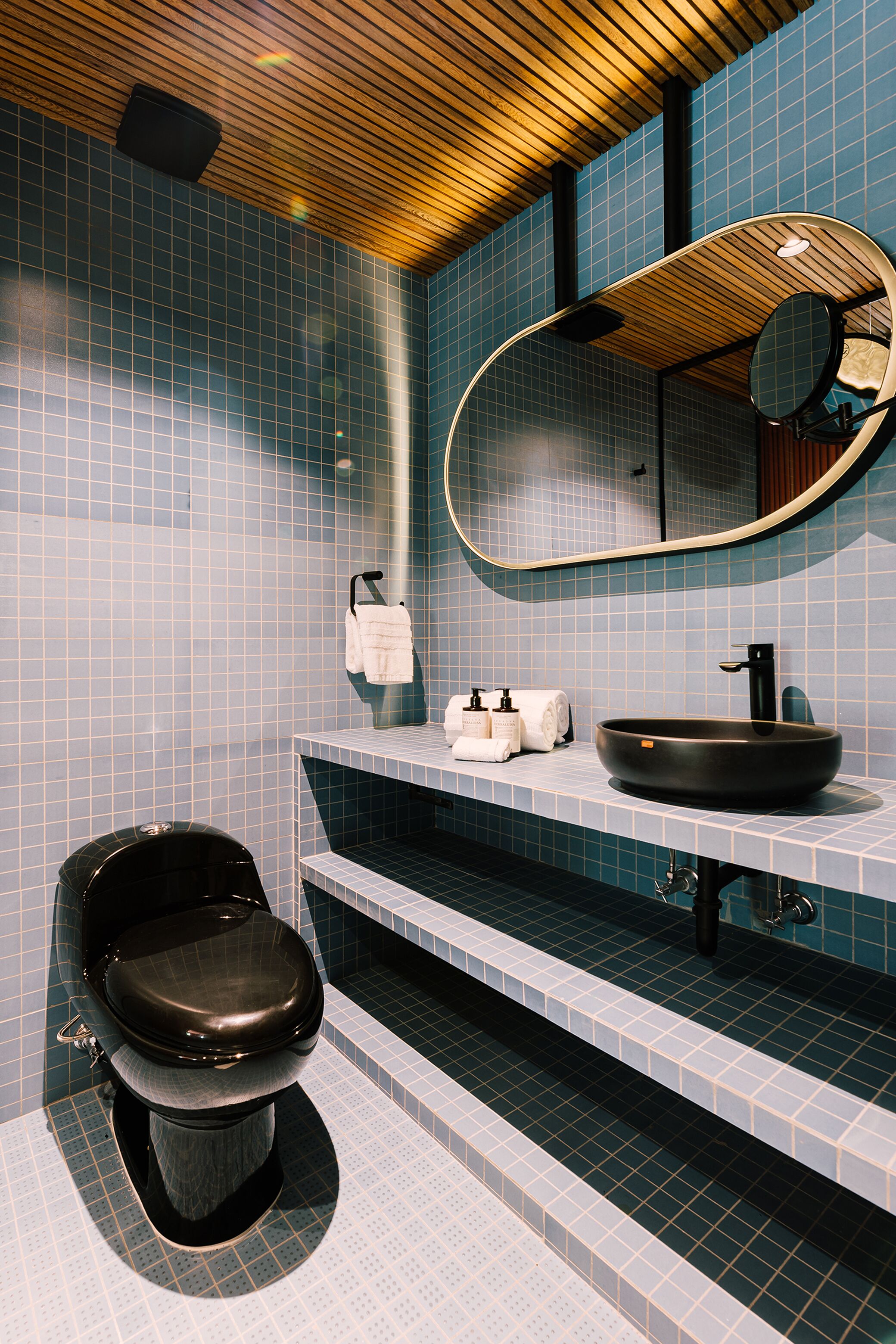 A modern bathroom with a black toilet, a round sink, and a mirror with a wooden frame.