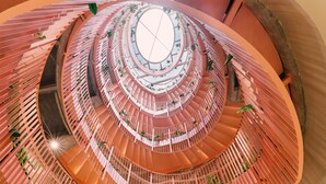 Un atrio de varios niveles con una escalera espiral central, rodeado de vegetación y un suelo con diseño.