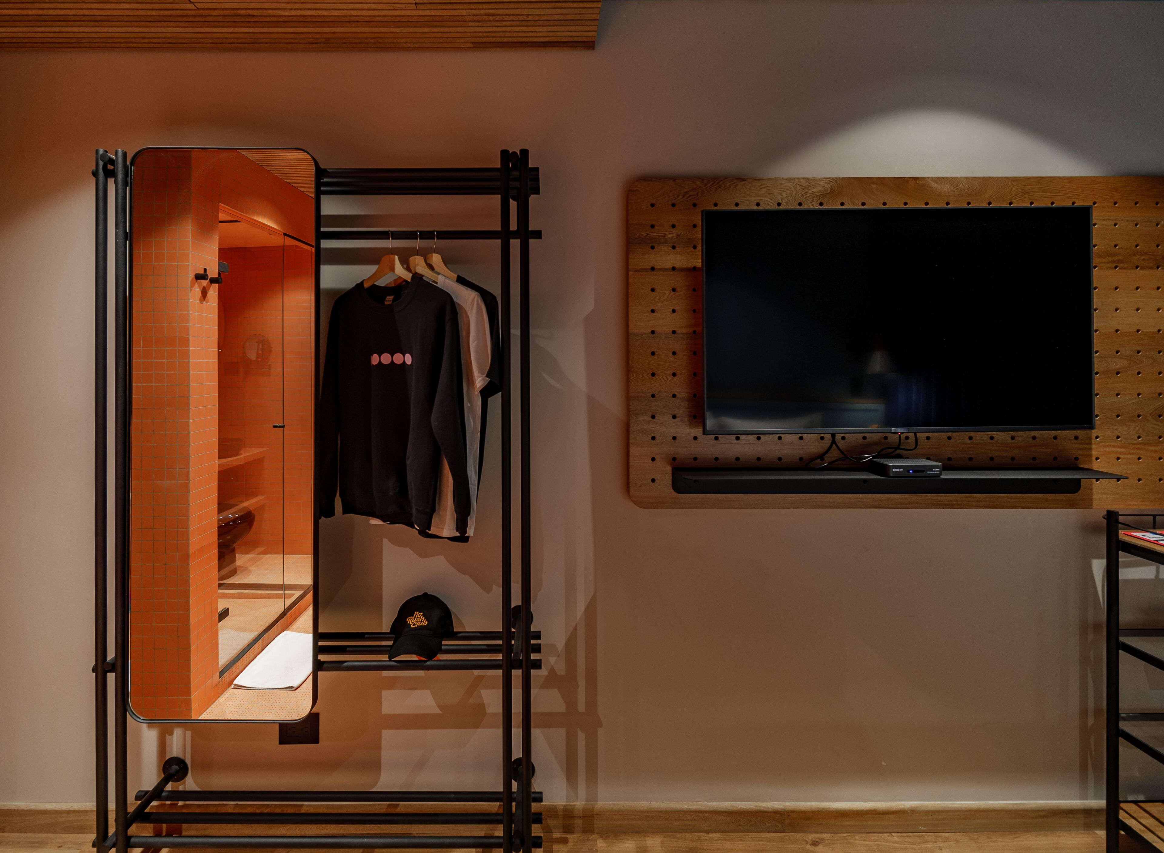 A room with a mirrored wardrobe, a television mounted on a wooden wall, and a shelf with a remote control.