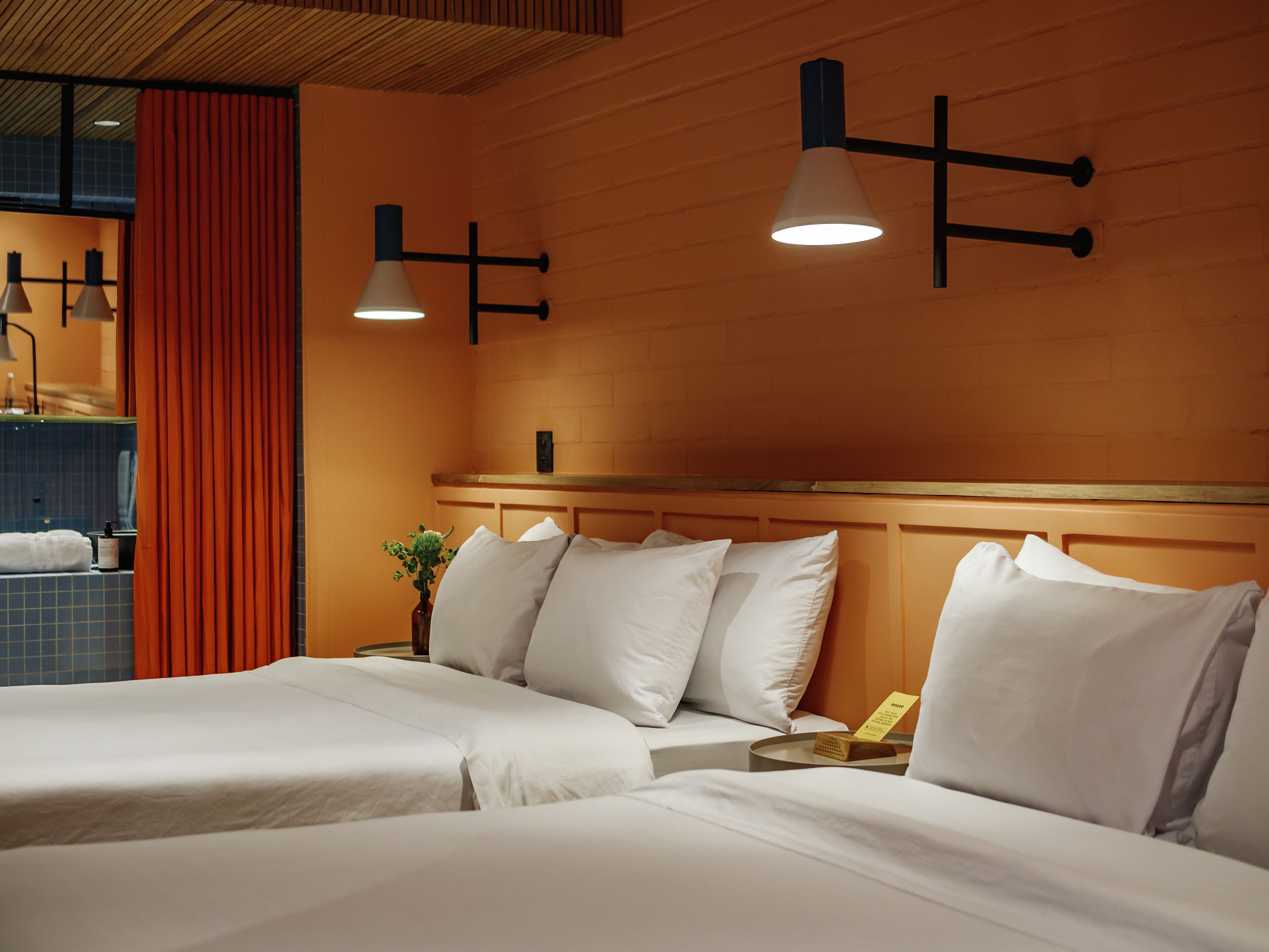 Una habitación de hotel con dos camas, cabecero de madera y lámparas colgantes.