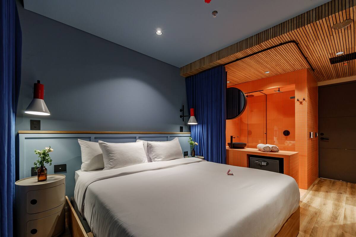 A modern bedroom with a large bed, bedside tables, and a bathroom visible through an open door.