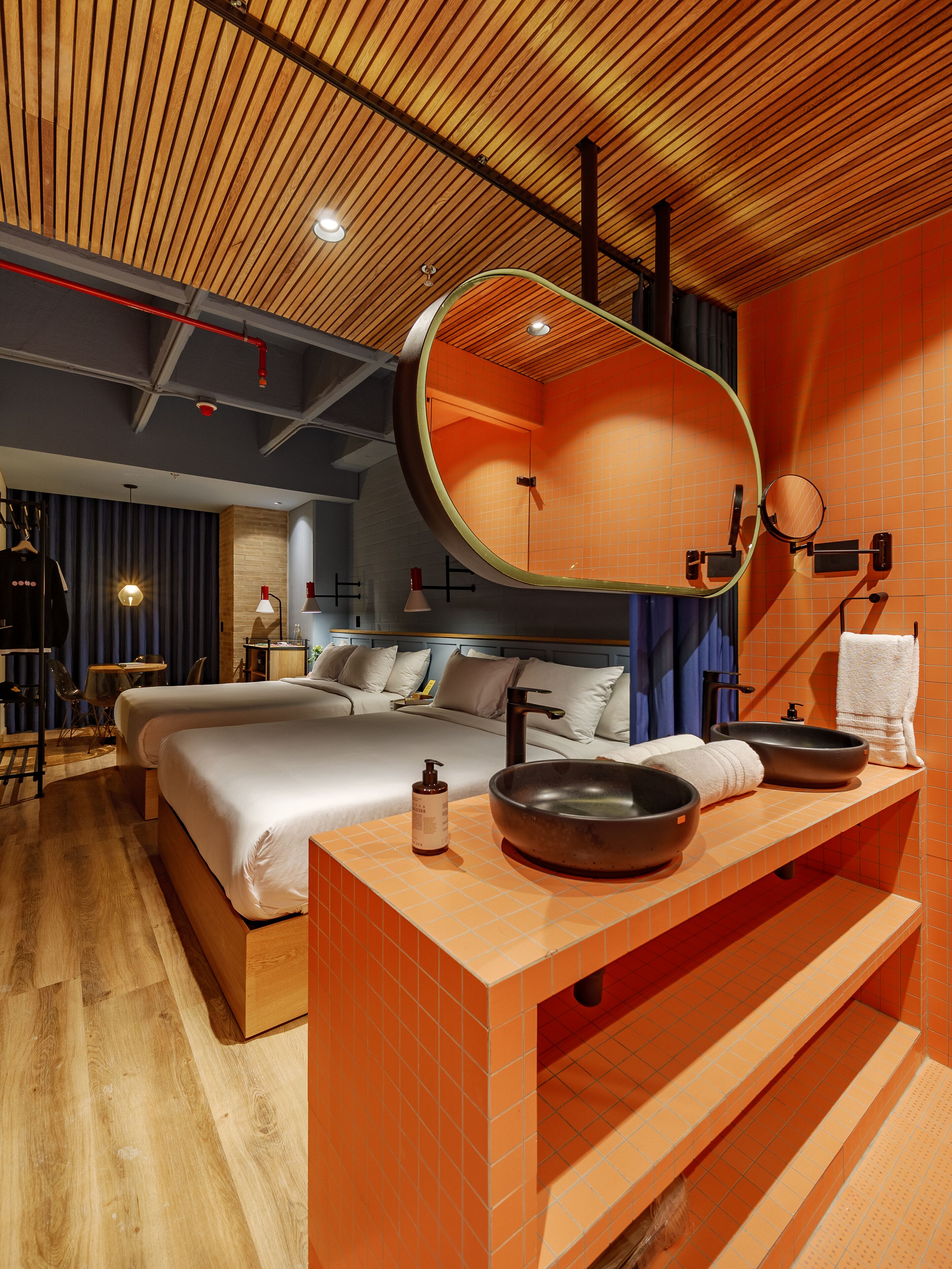 A modern hotel room with a large bed, a wooden ceiling, and a bathroom with a large mirror and two bowls on the sink.