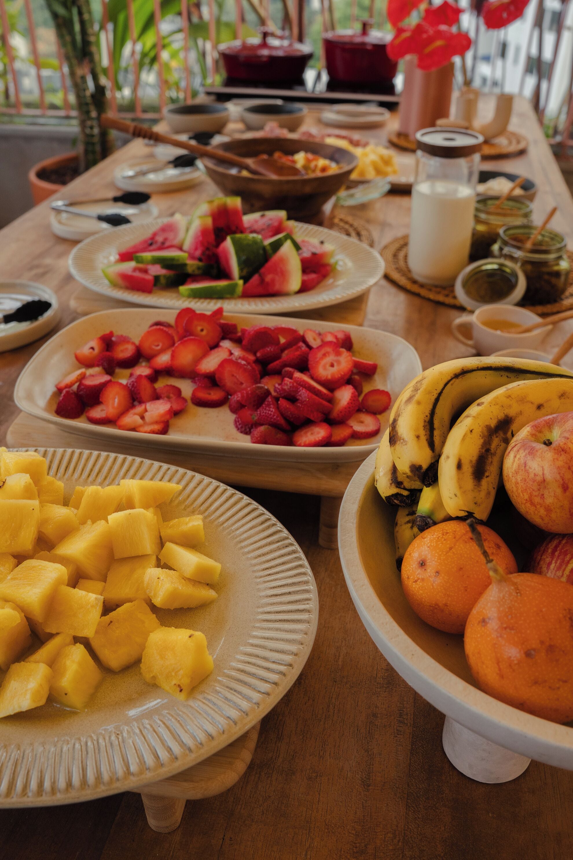 Una mesa con varias frutas y platos, incluyendo sandía, fresas, piña, plátanos y naranjas.