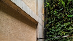 Un jacuzzi con cubierta de madera y un borde de hormigón, rodeado por un muro de ladrillo y una pared de follaje verde.
