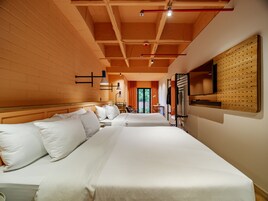 A hotel room with two beds, a wooden ceiling, a mounted TV, and a wall-mounted pegboard.