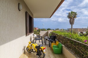 Un balcon avec un scooter jaune, des chaises noires et vertes, et une vue sur la mer.
