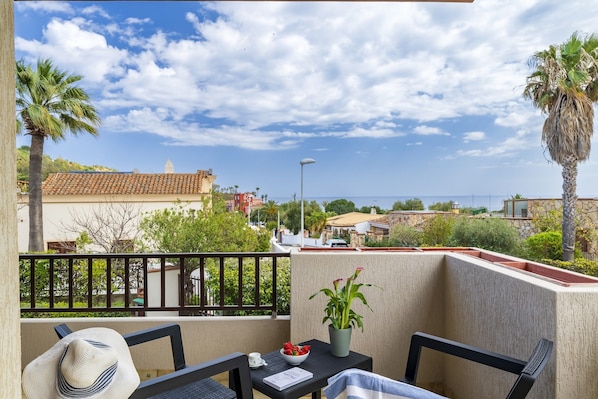 A balcony with a view of the sea, a table with a chair, a potted plant, and a hat. - Dependance Via Deffenu a 100 metri dalla spiaggia (Tortoli')