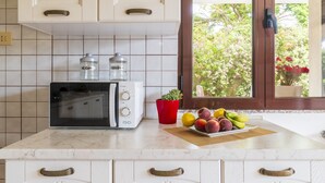 A kitchen with white cabinets, a microwave, a toaster, and a window with a view of trees and flowers. - Dependance Via Deffenu a 100 metri dalla spiaggia (Tortoli')