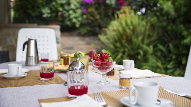 A breakfast table set with a coffee pot, a glass of red drink, a bowl of strawberries, a glass of juice, and a cup of coffee. - Dependance Via Deffenu a 100 metri dalla spiaggia (Tortoli')