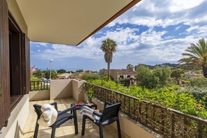 Ein Balkon mit Meerblick, einer Palme und einem Tisch mit Hut und Snacks.