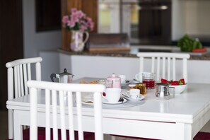 Une table à manger avec des chaises blanches, une théière, des tasses, un bol de fraises et un pot de miel.
