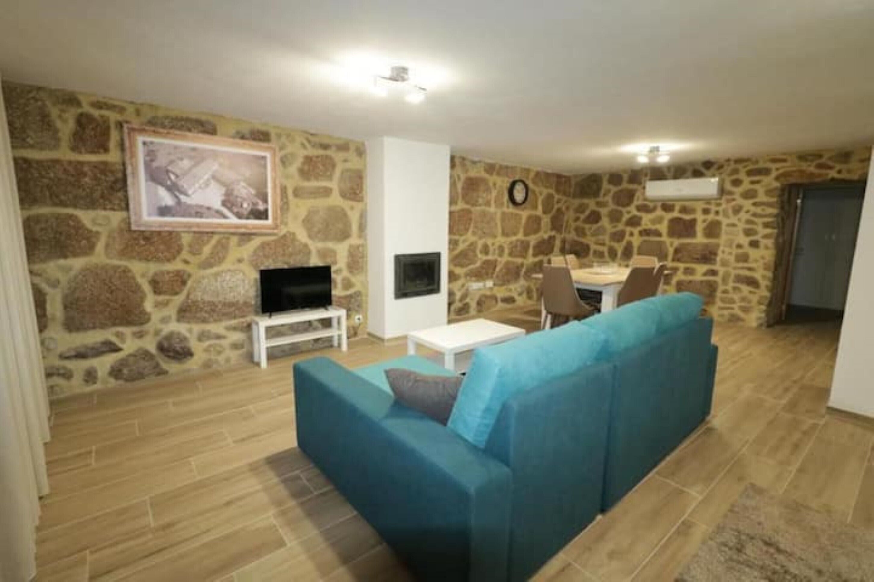 A living room with a stone wall, a blue sofa, a TV, and a dining table.