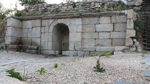 A stone structure with an arched entrance, surrounded by gravel and sparse vegetation.