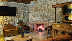 A cozy living room with a stone wall, a fireplace, wooden furniture, and a TV mounted on the wall.