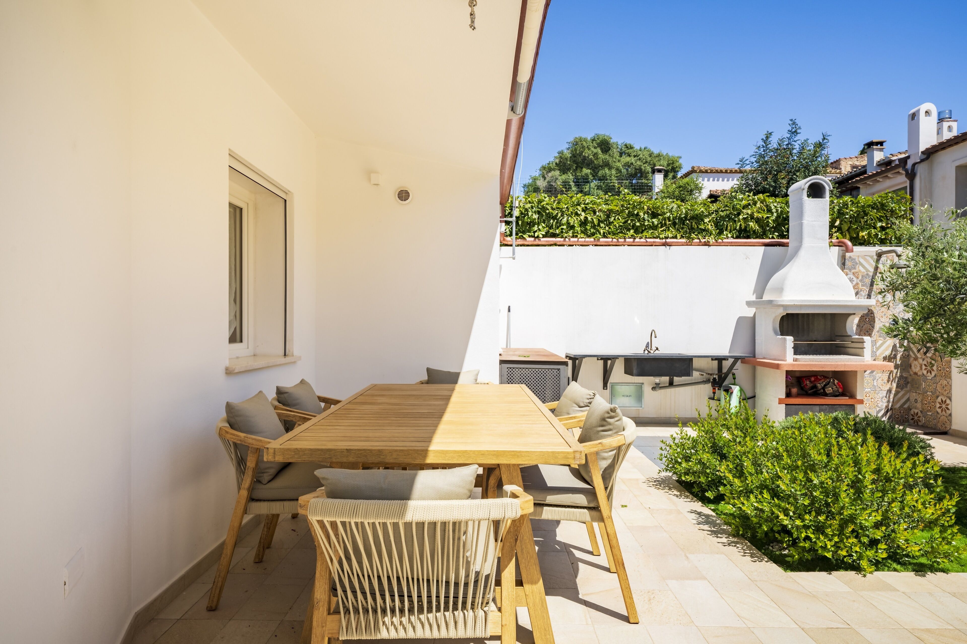 Un patio con una mesa y sillas de madera, una pared blanca y una chimenea.