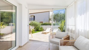 Ein modernes Wohnzimmer mit einer Couch, einem Couchtisch und einer Glastür, die auf eine Außenpatio mit Pool und Liegestühlen führt.