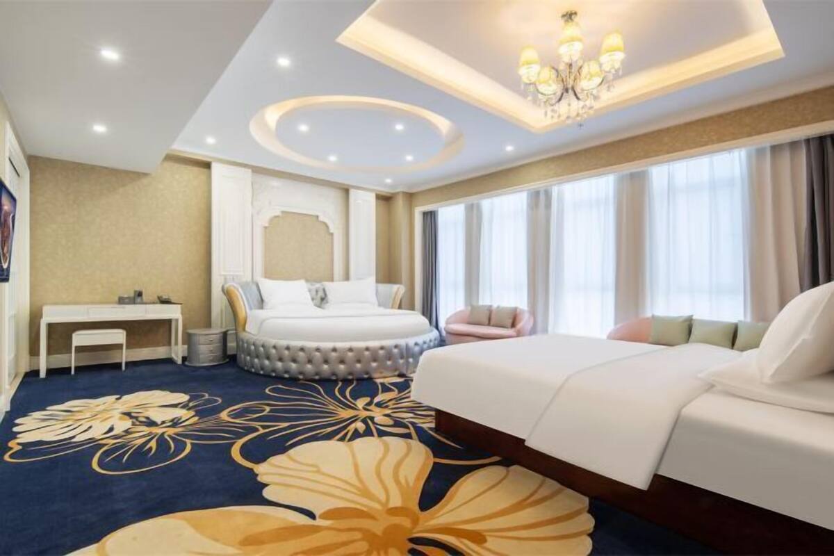 A hotel room with a large bed, a desk, a round seating area, and a chandelier.