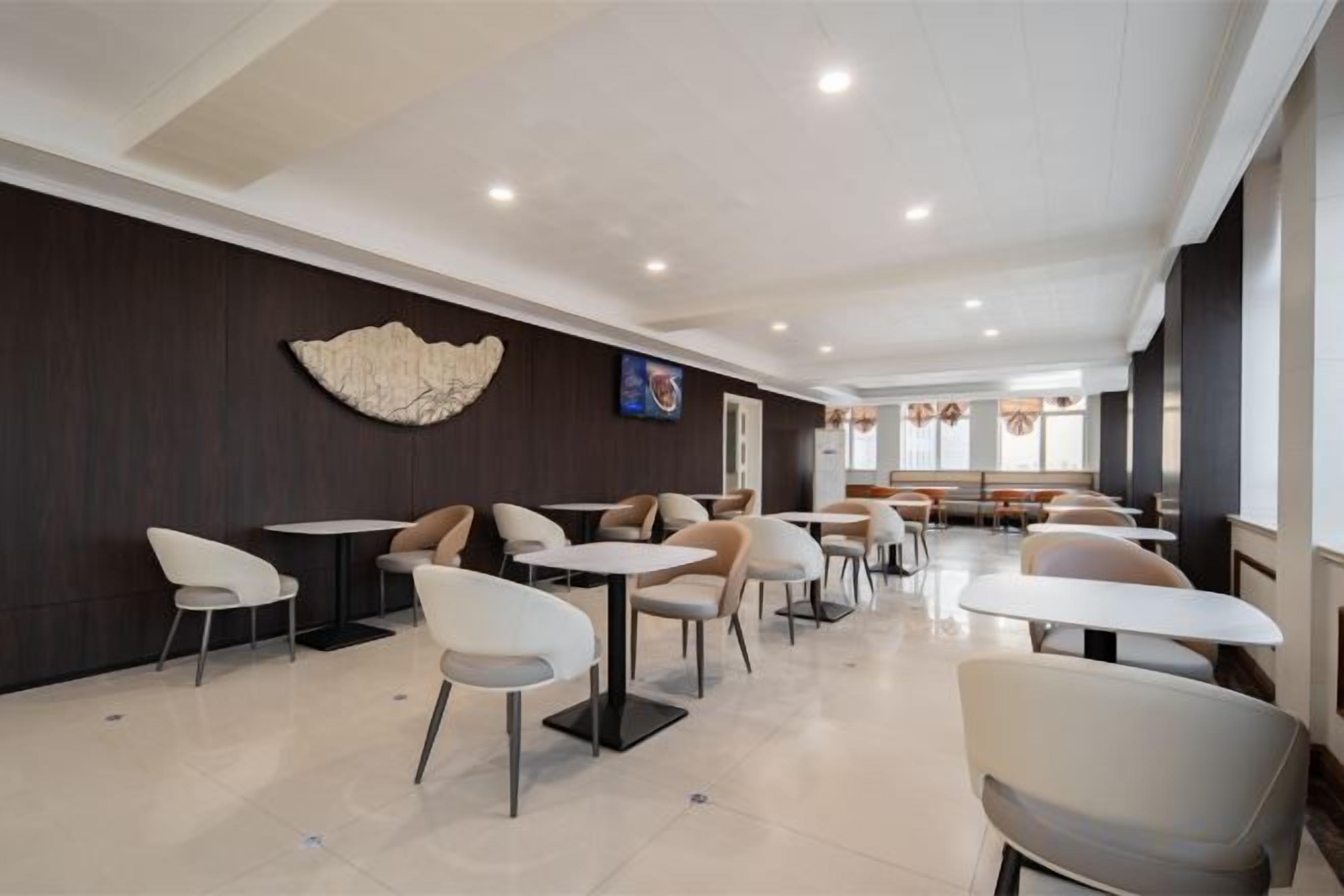 A modern dining area with tables and chairs, a decorative wall piece, and a seating area in the background.